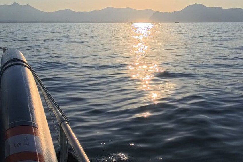 A boat's railing, calm water, and a sunset over mountains. 2