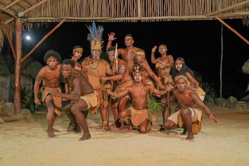A group of people in traditional attire posing under a thatched structure at night. 3