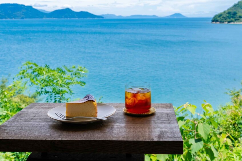 Una porción de pastel de queso en un plato y un vaso de té helado sobre una mesa de madera, con vistas a un lago y montañas al fondo. 4