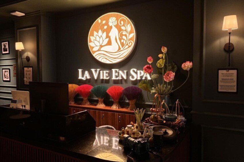 A spa reception area with a circular logo, a reception desk, and decorative flowers. 1