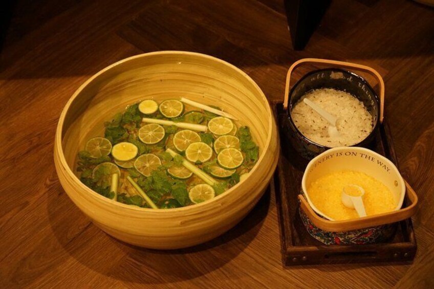 A bowl of soup with lime slices and herbs, a bowl of rice, and a container of yellow condiment on a wooden table. 4