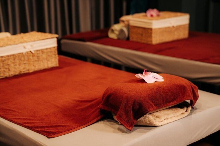 Two massage tables with red linens and a pink flower on one. 5