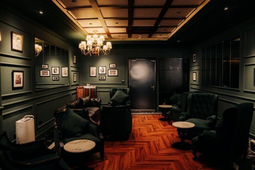 A dimly lit lounge with green walls, leather sofas, and a wooden parquet floor. 2