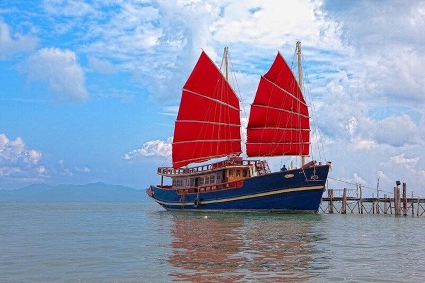 A traditional sailing boat with red sails on calm water, docked at a pier. 4