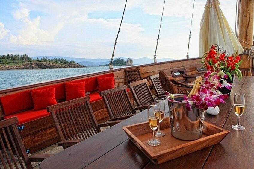 A wooden boat deck with red cushions, a table with drinks, and a bouquet of flowers. 3