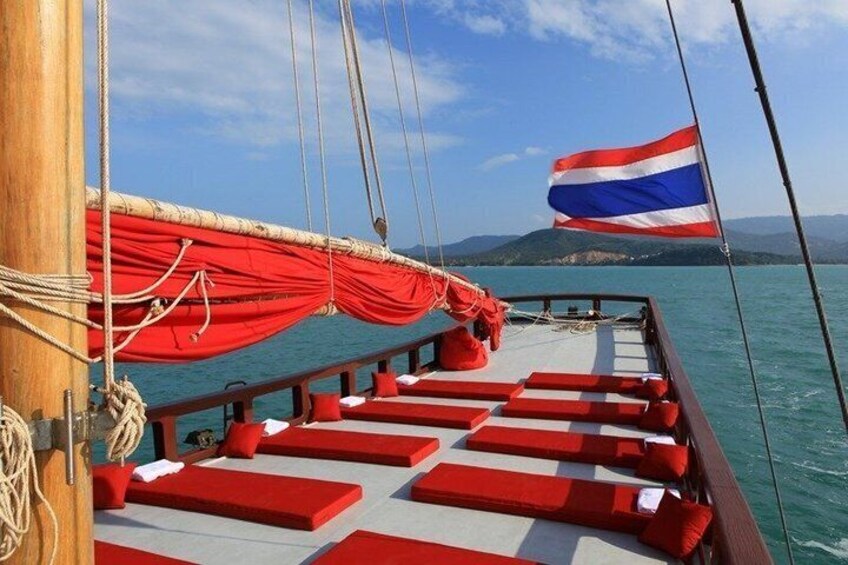 A boat deck with red cushions, a flag, and calm water. 1