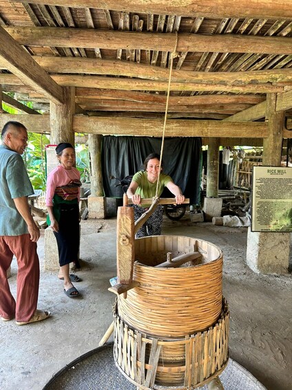 A traditional rice mill with a woman operating a wooden hand crank. 1