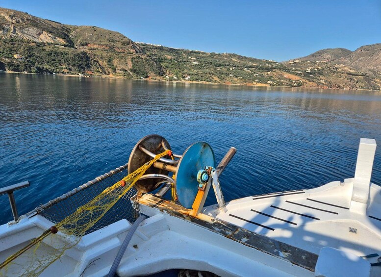 A boat with a net and winch on the deck, a calm lake, and hills in the background. 1