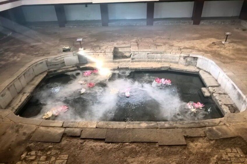 A hot spring with steam rising, surrounded by stone walls and a tiled floor. 5
