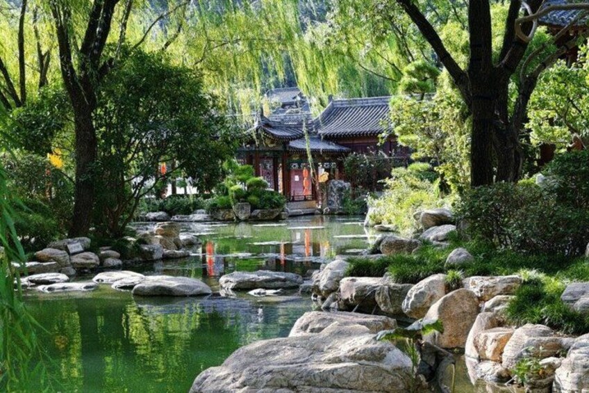 A traditional Japanese garden with a pond, rocks, trees, and a building in the background. 4