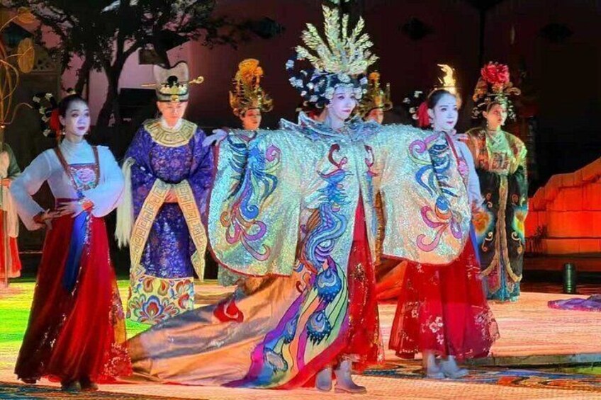 Performers in traditional costumes on a stage with elaborate headpieces and flowing garments. 1