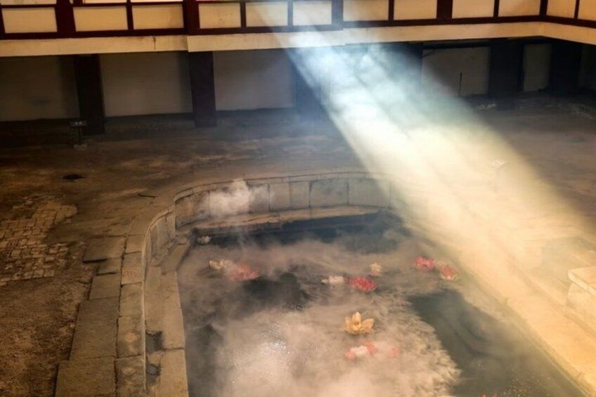A hot spring with steam rising, surrounded by stone walls and a wooden structure overhead. 3