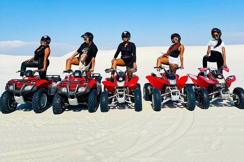 Five people on ATVs in a desert with sand dunes. 3