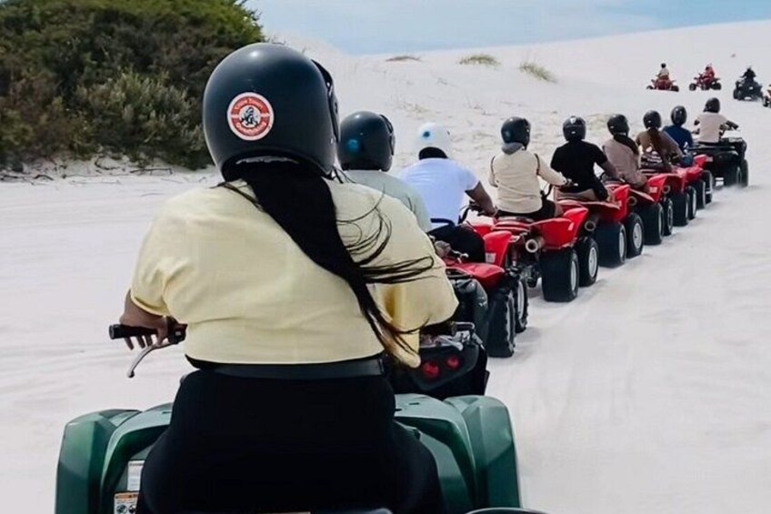 A group of people riding ATVs on a sandy path. 2