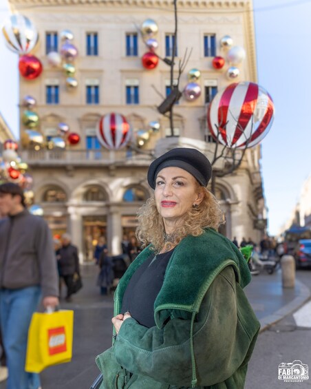 A person in a green coat and hat standing on a city street with festive decorations. 3