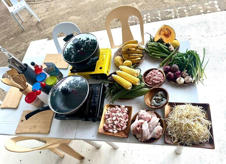 A table with various food items and cooking utensils, including a frying pan, bowls of diced meat, and fresh vegetables like corn and green beans. 2