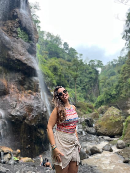 A person standing in front of a waterfall with lush greenery in the background. 4