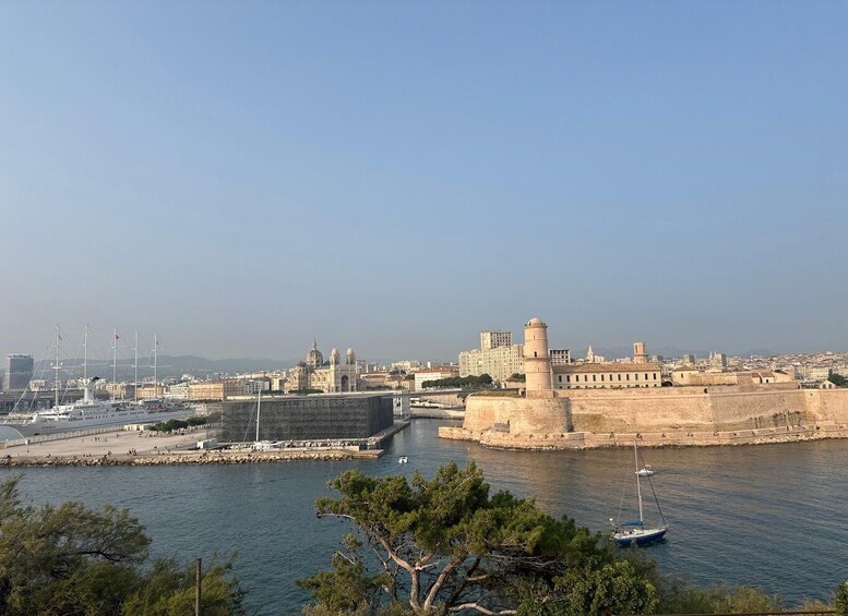 A coastal cityscape with a prominent historic fort, a marina with boats, and a clear sky. 3