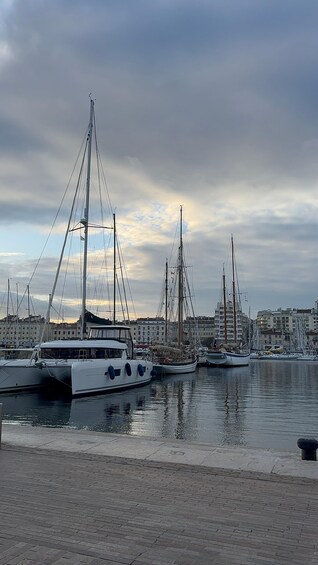 A marina with several sailboats docked, a cloudy sky, and buildings in the background. 5
