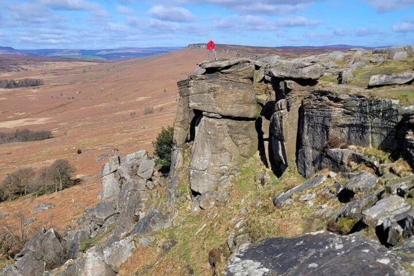 A rocky outcrop with a red flag, a vast open landscape, and distant hills. 3