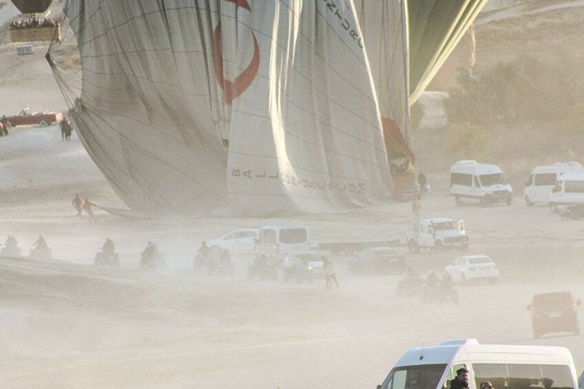 A sailboat with a red logo on its sail, surrounded by vehicles on a sandy beach. 1