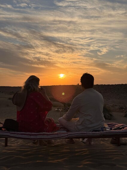 Two people sitting on a bench facing a sunset over a desert landscape. 2