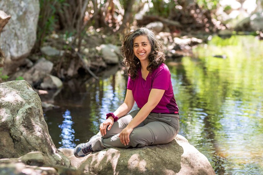 A person sitting on a rock by a calm body of water surrounded by rocks and greenery. 5