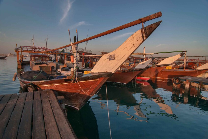 A dock with several boats tied up, wooden planks, and a clear sky. 1