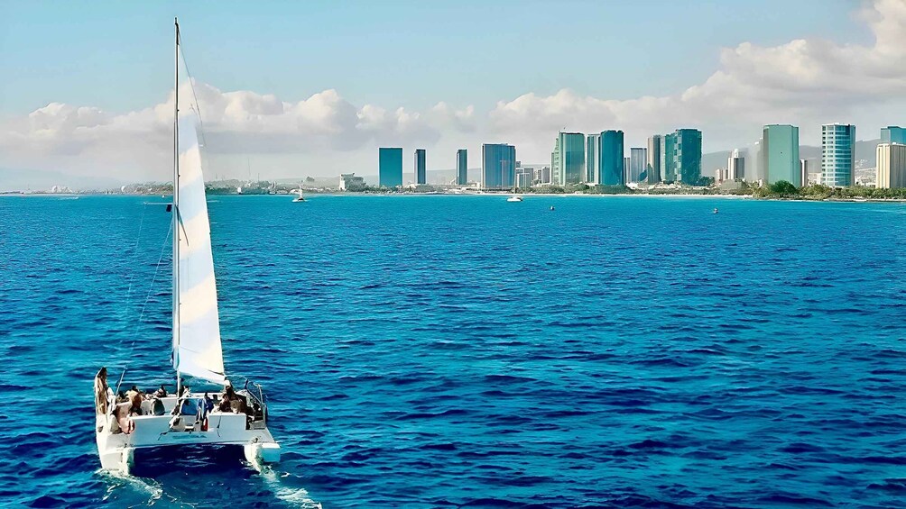 A sailboat on a blue sea with a city skyline in the background. 1