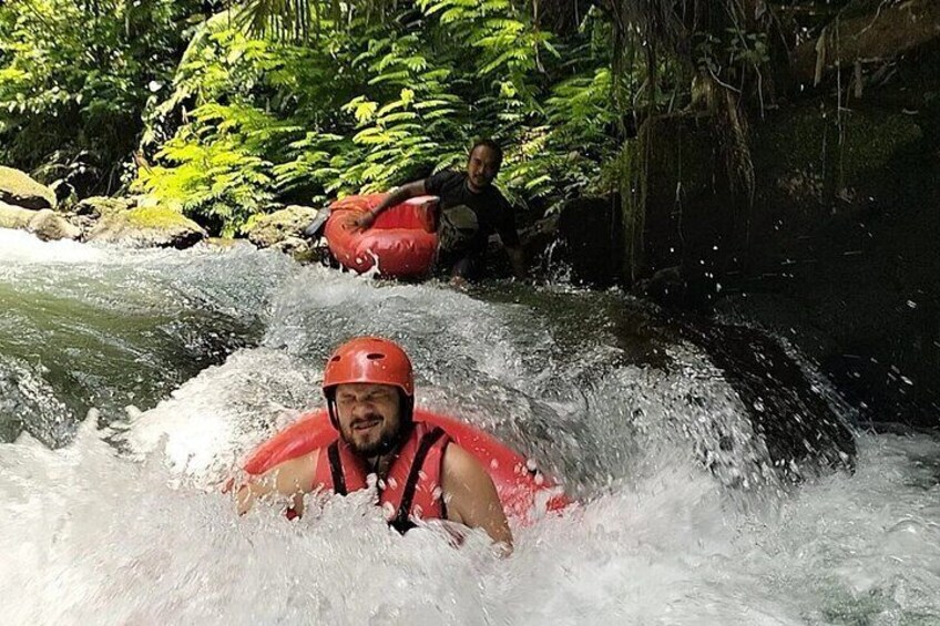 A person in a red helmet and life jacket on a river, with another person in the background. 2
