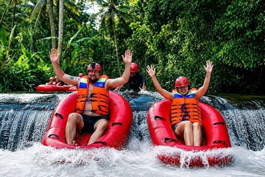 Two people in red inflatable tubes sliding down a waterfall in a forested area. 4