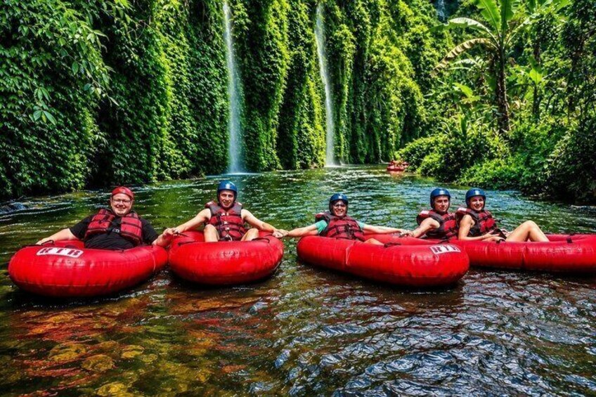 People in red inflatable tubes on a river surrounded by dense greenery and a waterfall. 1