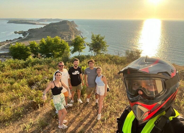 A group of people on a hillside with a sunset over the ocean. 4