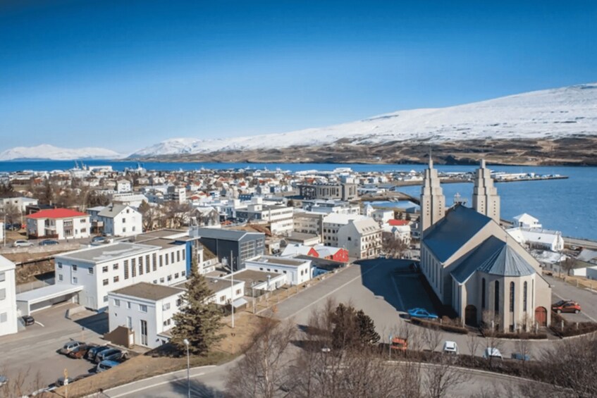 A town with a church, a body of water, and snow-capped mountains in the background. 3