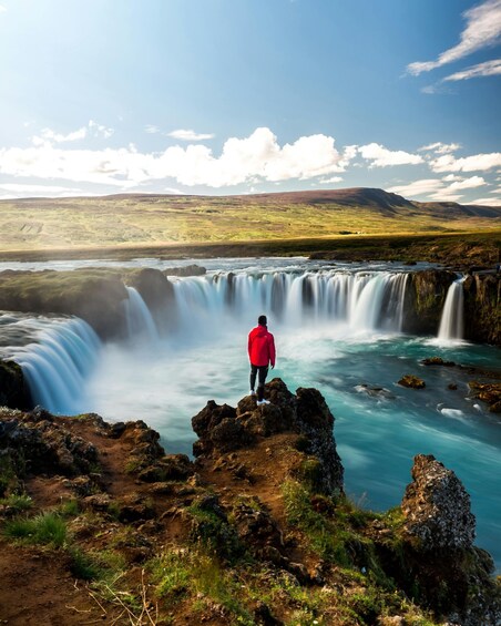 A person in a red jacket standing on a rocky outcrop overlooking a waterfall. 2