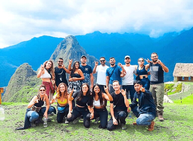 A group of people posing in front of a mountainous landscape with a thatched-roof structure in the background. 3