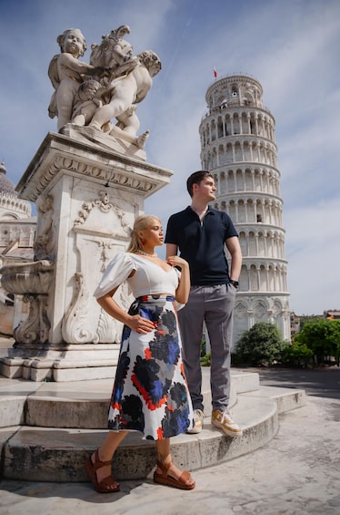 A couple standing in front of the Leaning Tower of Pisa with a sculpture of cherubs behind them. 5