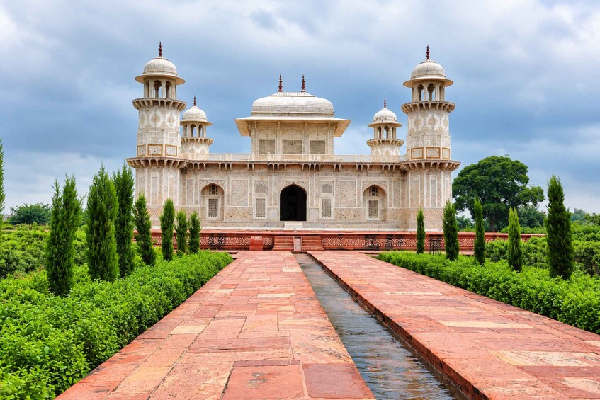 A white marble mausoleum with four domes and two minarets, surrounded by lush greenery and a water channel. 5