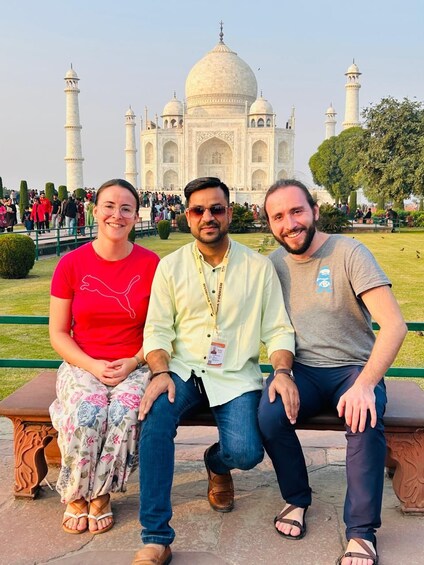 Three people sitting on a bench with the Taj Mahal in the background. 4