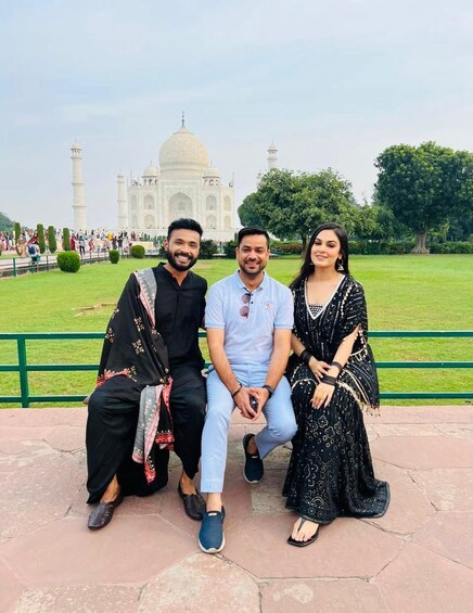 Three people sitting on a bench with the Taj Mahal in the background. 3
