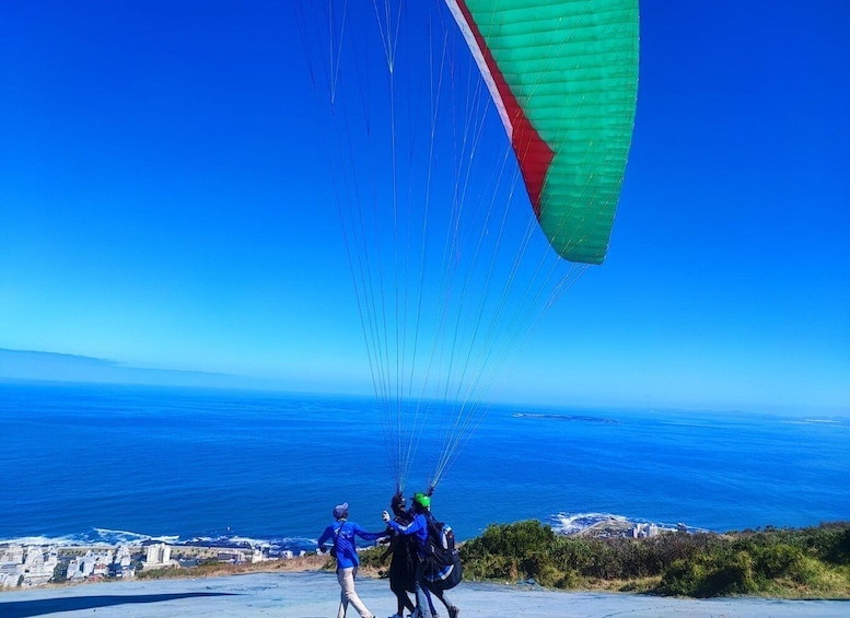 Due persone che volano in parapendio con un paracadute verde e rosso sopra un paesaggio costiero. 1