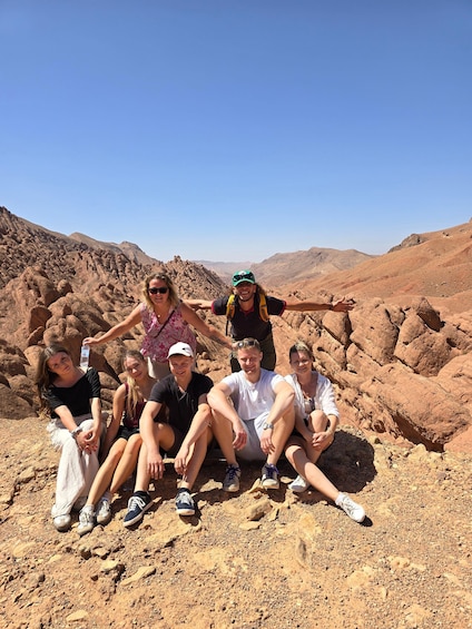 A group of people sitting on rocky terrain with a desert landscape in the background. 5