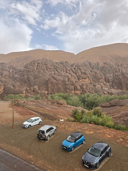 A parking area with four cars and a rocky landscape in the background. 2