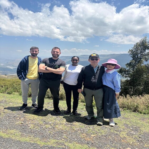A group of five people standing on a rocky outcrop with a scenic view of a valley and mountains in the background. 3