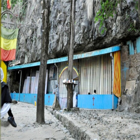 A rocky terrain with a building featuring a blue and yellow facade, a tree, and a flag. 4