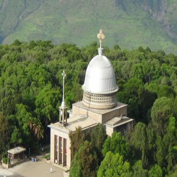 A white dome structure with a golden cross on top, surrounded by lush greenery. 2