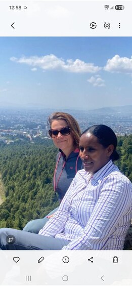 Two people sitting on a bench overlooking a forested landscape with a city in the distance. 2