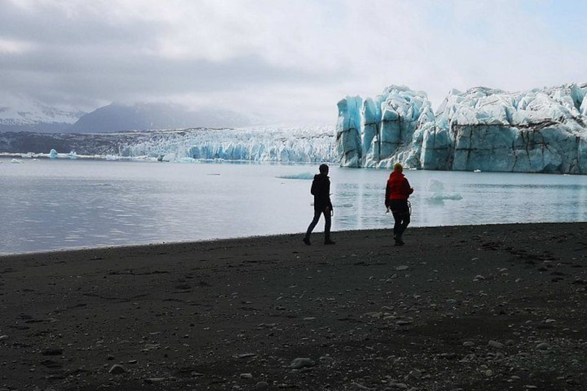 A glacier with people walking on a rocky shore. 4