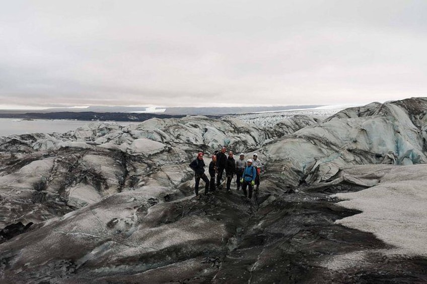 A group of people hiking on a glacier with a body of water in the background. 2