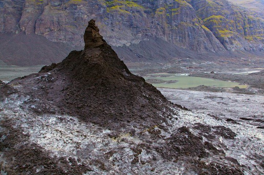 A rugged mountain peak with a distinct conical shape, surrounded by a barren landscape with sparse vegetation and distant mountains. 1